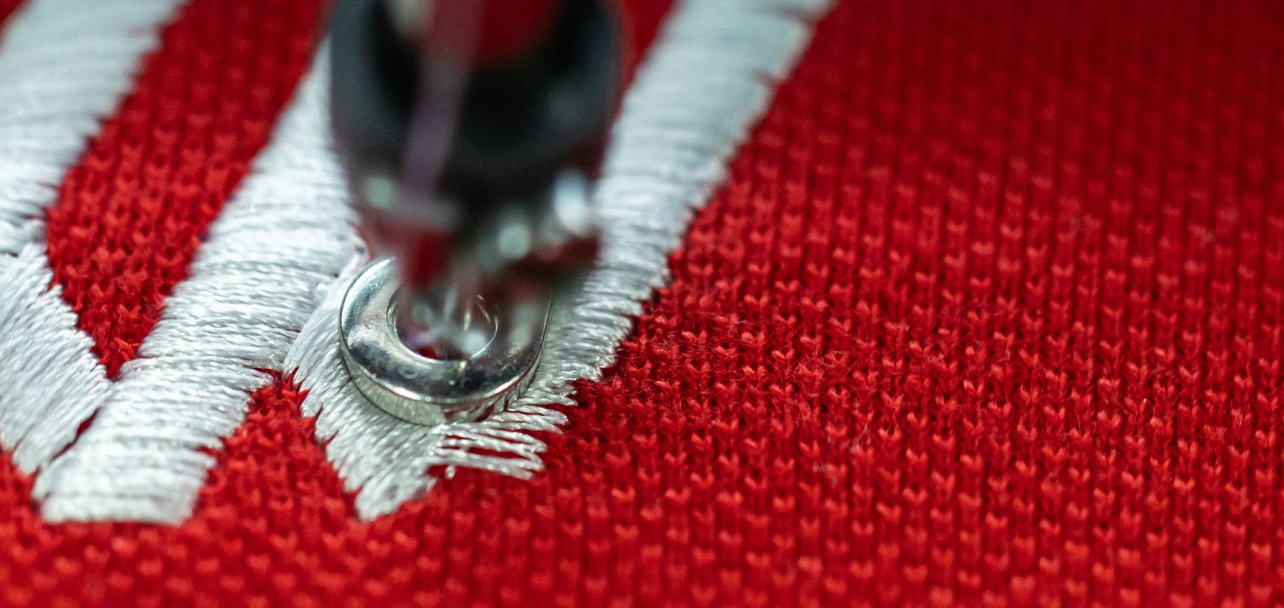 Embroidery machine stitching white thread into red knit fabric in close-up.